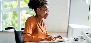 Mulher negra, com cabelo preso, olhando para a tela do computador.
