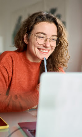 Mulher branca, com cabelo longo e óculos, sorrindo olhando para a tela do notebook.